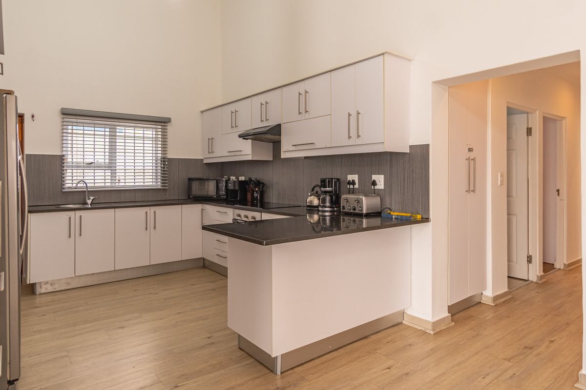Modern kitchen featuring white cabinetry, dark granite countertops, stainless steel sink, extractor fan, and light wood-look laminate flooring.