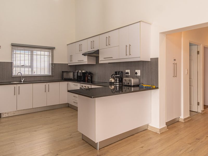 Modern kitchen featuring white cabinetry, dark granite countertops, stainless steel sink, extractor fan, and light wood-look laminate flooring.