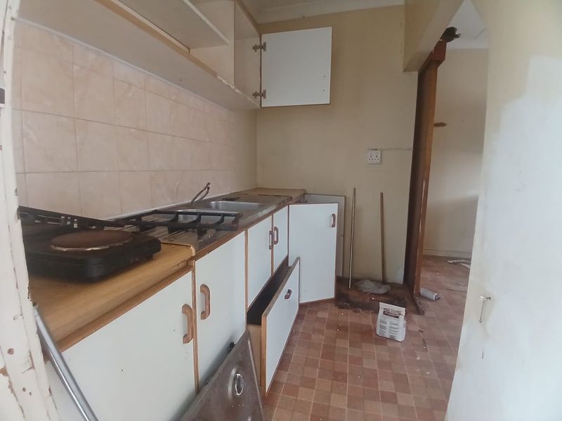 A dated kitchen space featuring original cabinetry, a gas hob, and tiled backsplash, currently in need of renovation and modernization.