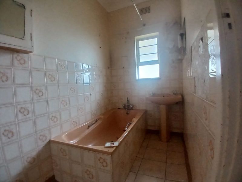 A dated bathroom featuring a built-in bathtub and pedestal basin, requiring renovation and cosmetic updates to improve its condition and appeal.