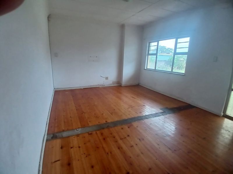 An empty living room featuring polished timber flooring and a large window, requiring minor repairs to the floor and wall finishes.