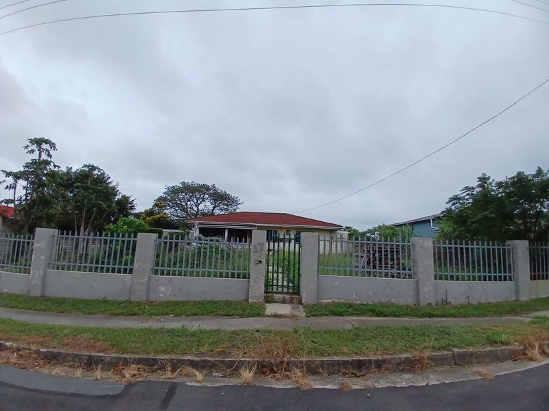 Front view of a residential property featuring a perimeter concrete wall, metal fencing, and a gated entrance with a tiled roof house visible behind.
