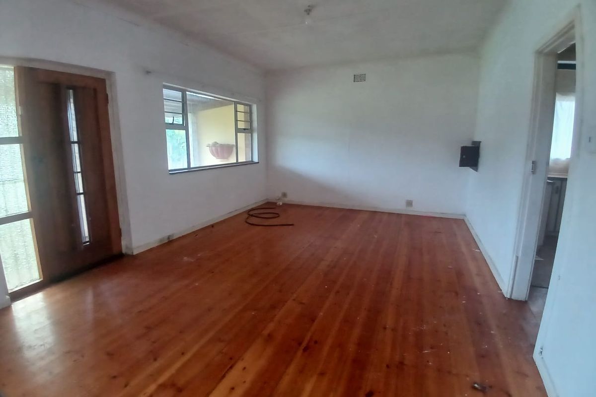 An empty living room featuring polished timber flooring, a wooden entrance door, and large windows providing natural light.
