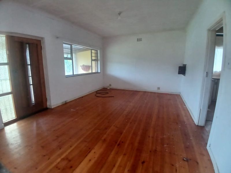 An empty living room featuring polished timber flooring, a wooden entrance door, and large windows providing natural light.