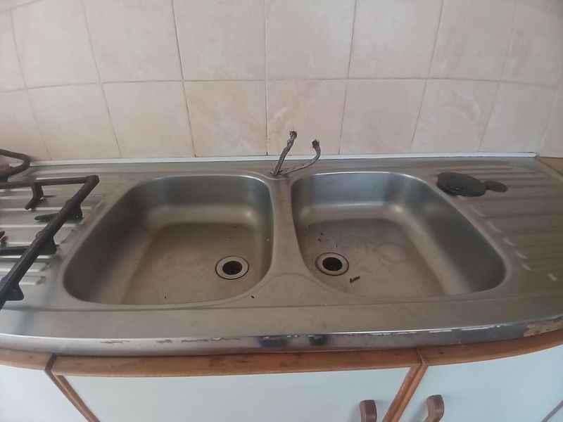 A kitchen sink area featuring a double bowl stainless steel sink, integrated gas hob, and tiled splashback, currently requiring maintenance and fixture replacement.