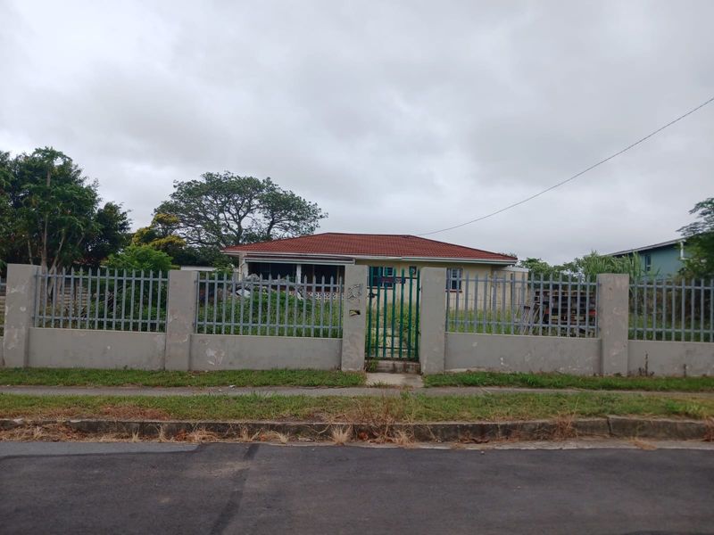 Front view of a single-story house featuring a tiled roof, enclosed by a perimeter wall with metal security fencing and a pedestrian gate.