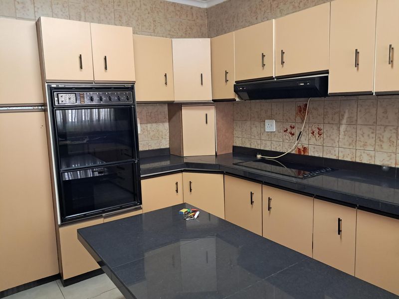 A functional kitchen featuring dark stone countertops, built-in oven, electric hob, extractor fan, and ample laminate cabinetry with a tiled backsplash.