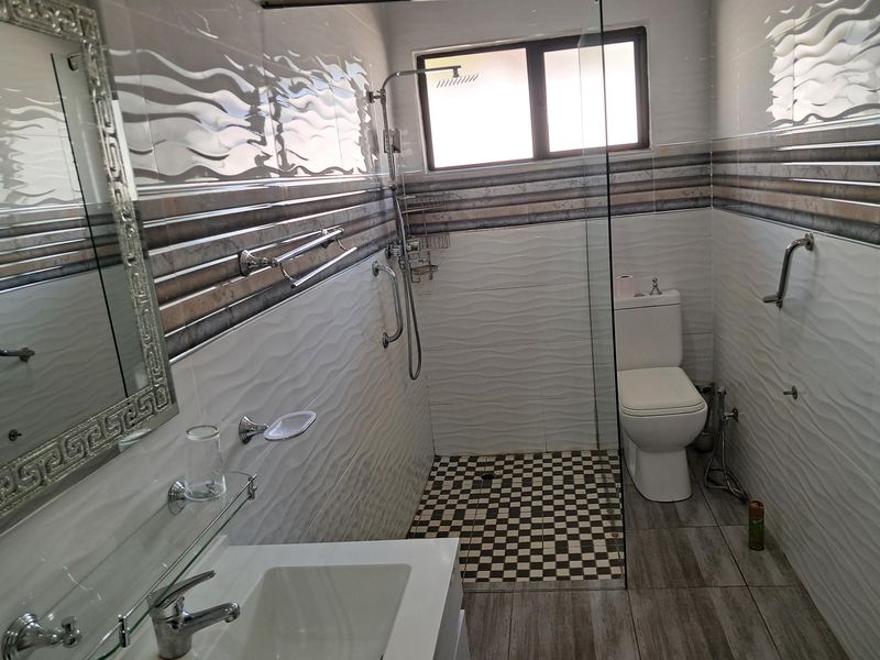 A modern, well-maintained bathroom featuring a glass-enclosed shower, contemporary wall tiling, a vanity basin, and accessible grab rails.