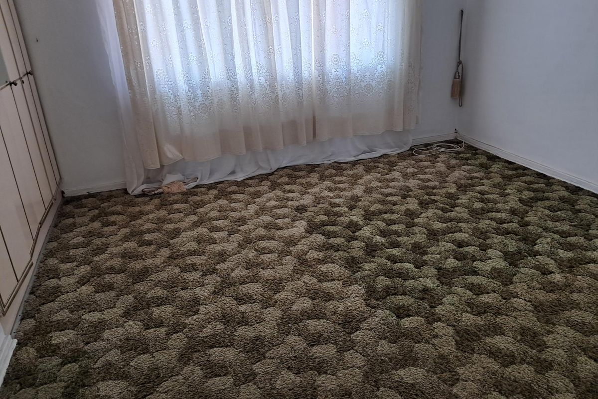 A vacant bedroom featuring built-in wardrobe storage and dated textured carpet flooring.