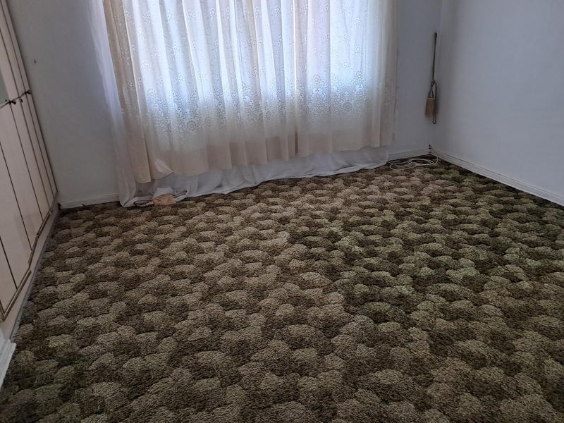 A vacant bedroom featuring built-in wardrobe storage and dated textured carpet flooring.