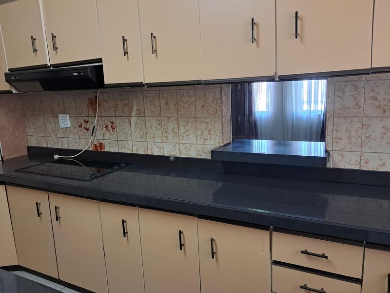 A functional kitchen featuring built-in cabinetry, dark stone countertops, an integrated electric hob, and an extractor fan with a tiled backsplash.