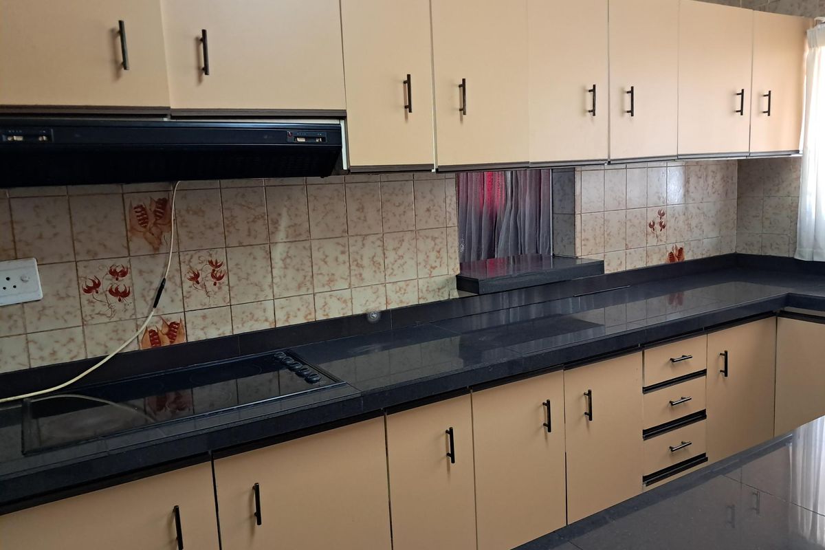 A functional kitchen featuring extensive built-in cabinetry, dark laminate countertops, a built-in electric hob with extractor fan, and decorative ceramic tile backsplash.