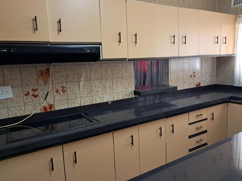 A functional kitchen featuring extensive built-in cabinetry, dark laminate countertops, a built-in electric hob with extractor fan, and decorative ceramic tile backsplash.