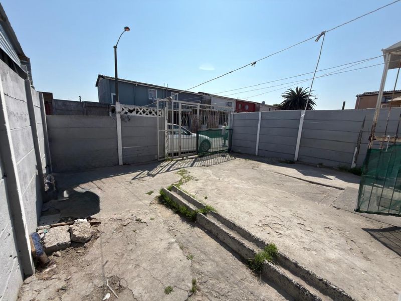 A paved rear courtyard area enclosed by concrete boundary walls and a metal security gate, offering a functional outdoor space.
