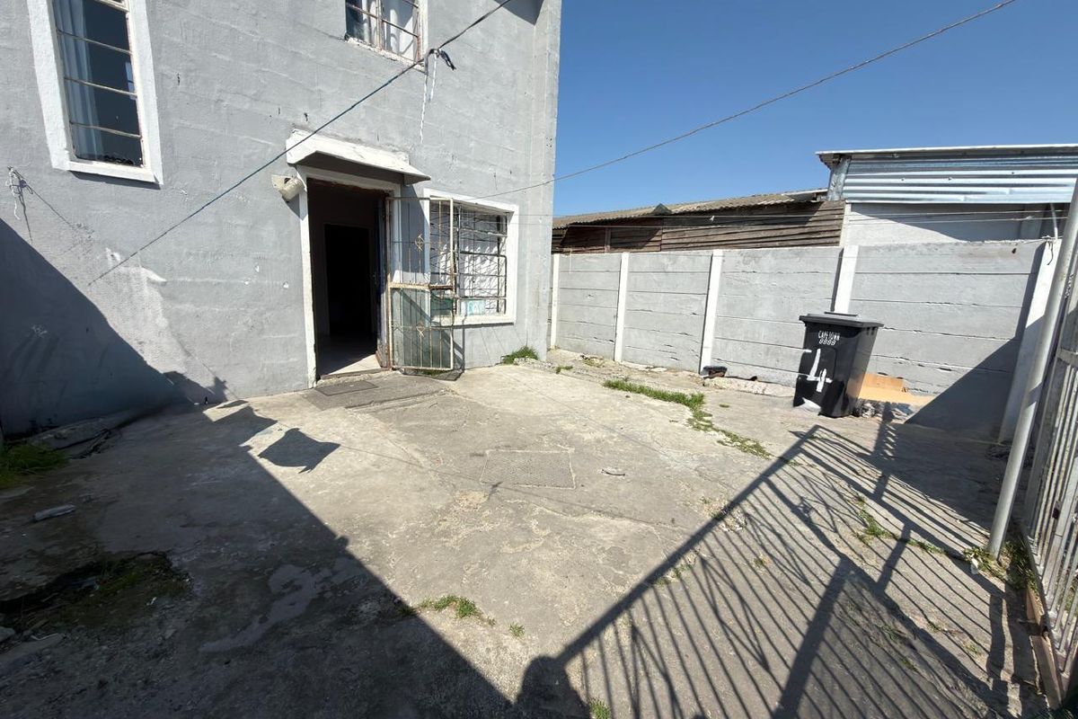 Rear exterior area featuring concrete paving, a precast boundary wall, and direct access to the main dwelling through a security gate.
