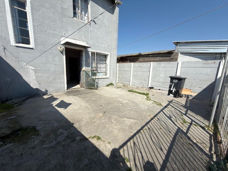 Rear exterior area featuring concrete paving, a precast boundary wall, and direct access to the main dwelling through a security gate.