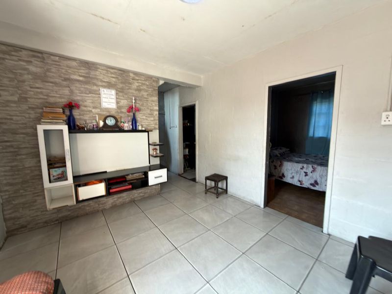Living room featuring tiled flooring and a stone-cladding feature wall with a built-in media unit, providing access to adjacent rooms.