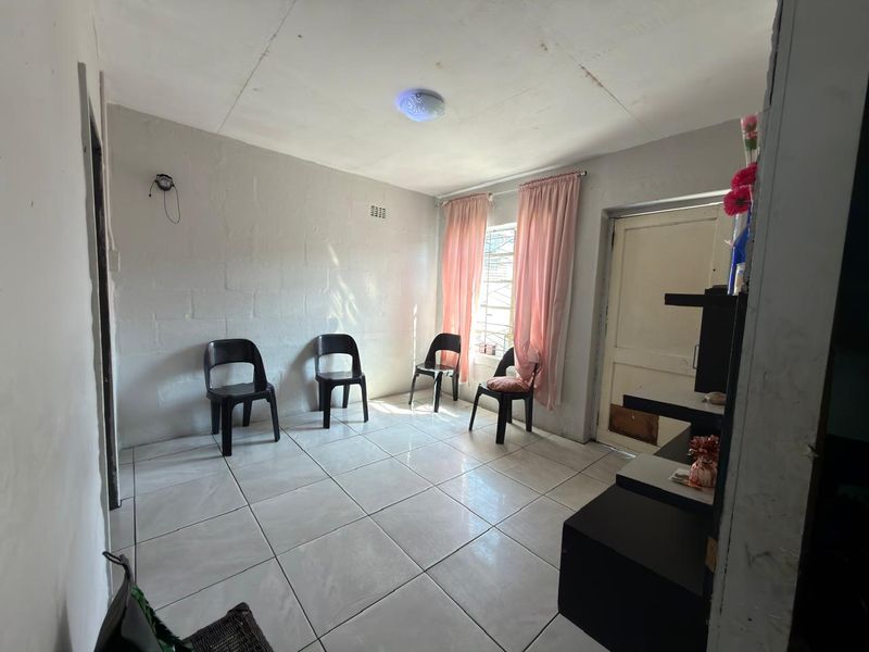A simple living area featuring tiled flooring, exposed blockwork walls, and a standard ceiling light fixture, offering a blank canvas for potential renovation.