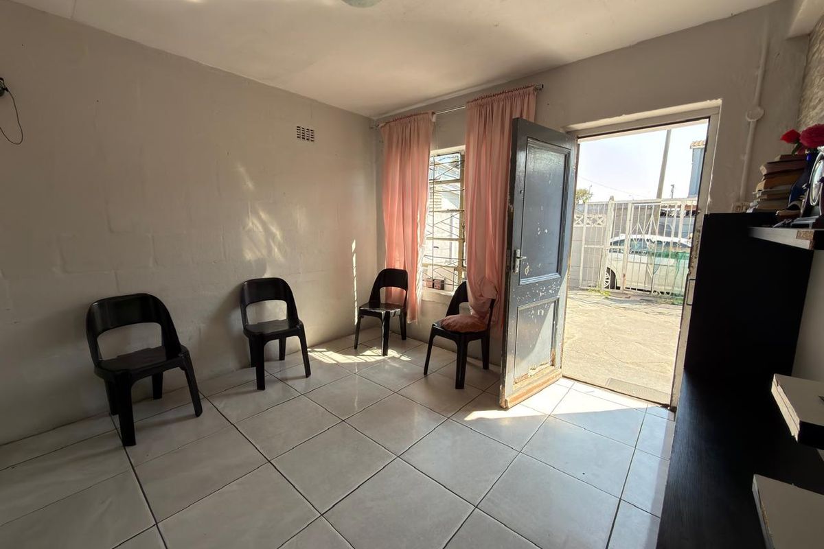 A simple living area featuring tiled flooring, natural light through an external door, and security bars on the window.