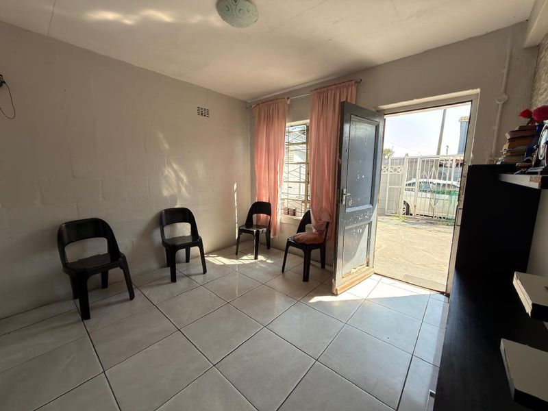 A simple living area featuring tiled flooring, natural light through an external door, and security bars on the window.