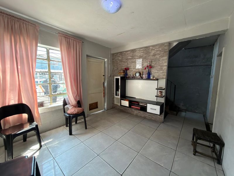 A living room featuring tiled flooring, a built-in media unit, and a staircase, with potential for cosmetic updates to improve the overall finish.