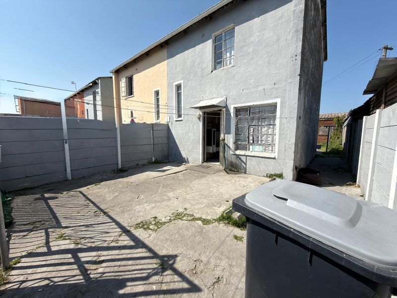 Rear exterior view of the property featuring a concrete paved courtyard, precast boundary walls, and a two-story building facade with steel-framed windows.