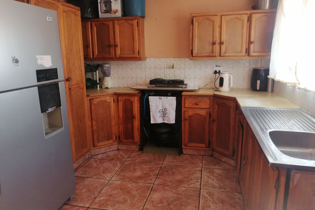 A dated kitchen featuring wooden cabinetry, tiled flooring, and a stainless steel sink, offering significant potential for modernization and renovation.