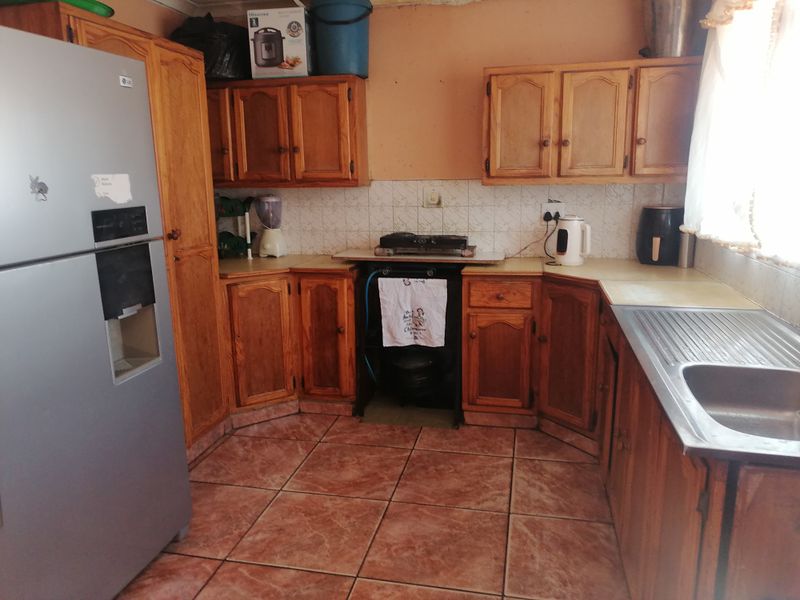 A dated kitchen featuring wooden cabinetry, tiled flooring, and a stainless steel sink, offering significant potential for modernization and renovation.