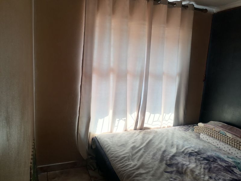 A bedroom featuring tiled flooring and a window with a curtain rod, providing natural light.
