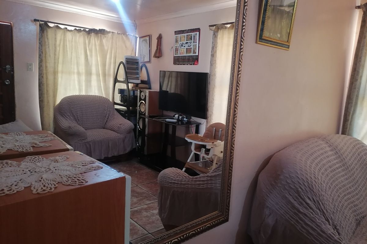 A living room area featuring tiled flooring and a large wall-mounted mirror, providing a functional space for relaxation.