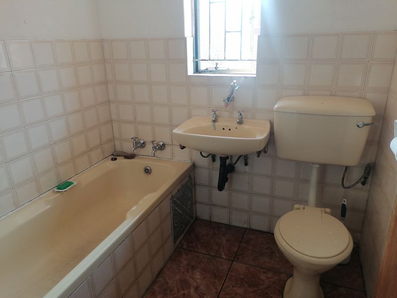 A dated bathroom featuring a bathtub, wall-mounted basin, and toilet with original ceramic tiling throughout.