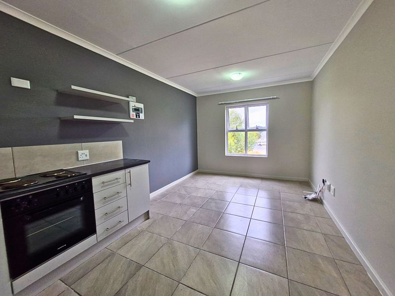 An open-plan living and kitchen area featuring tiled flooring, built-in oven and hob, and neutral wall finishes.