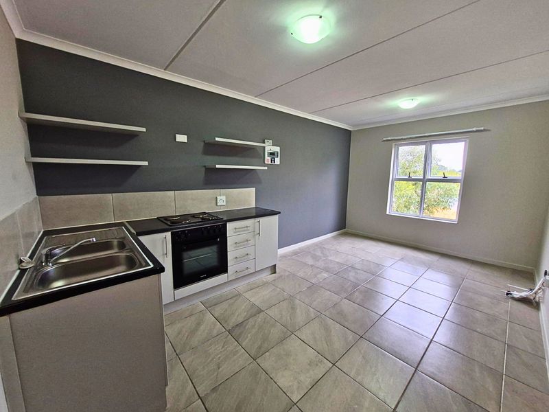 An open-plan kitchen area featuring tiled flooring, built-in cabinetry, a stainless steel sink, and an integrated oven with hob.