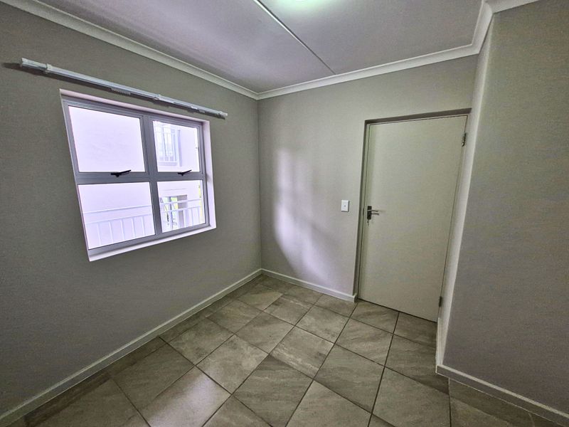 A clean, empty bedroom featuring neutral wall paint, tiled flooring, and a window with a curtain rail.