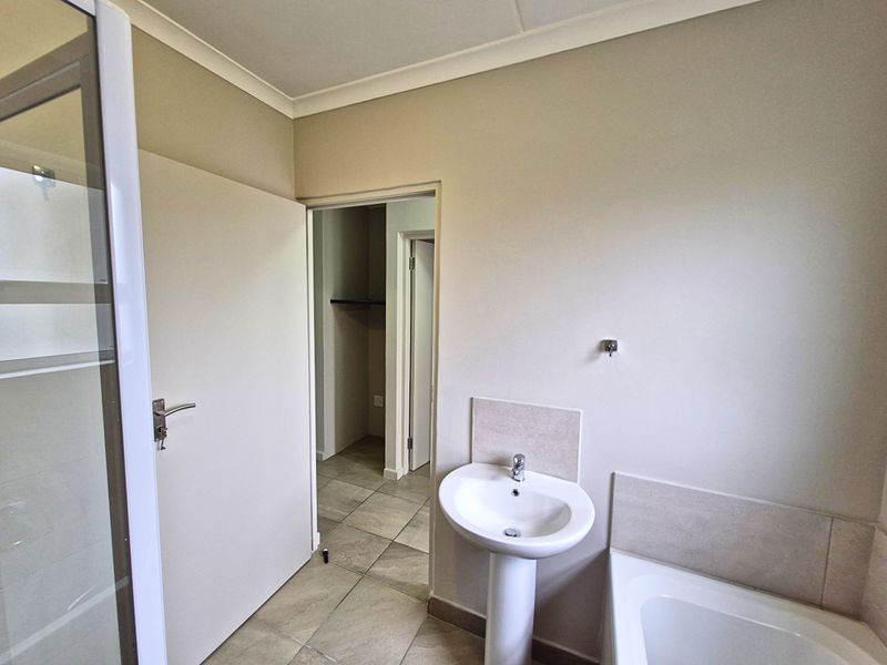 A clean, functional bathroom featuring a pedestal basin, bathtub, and separate shower enclosure with neutral tiled flooring and wall finishes.