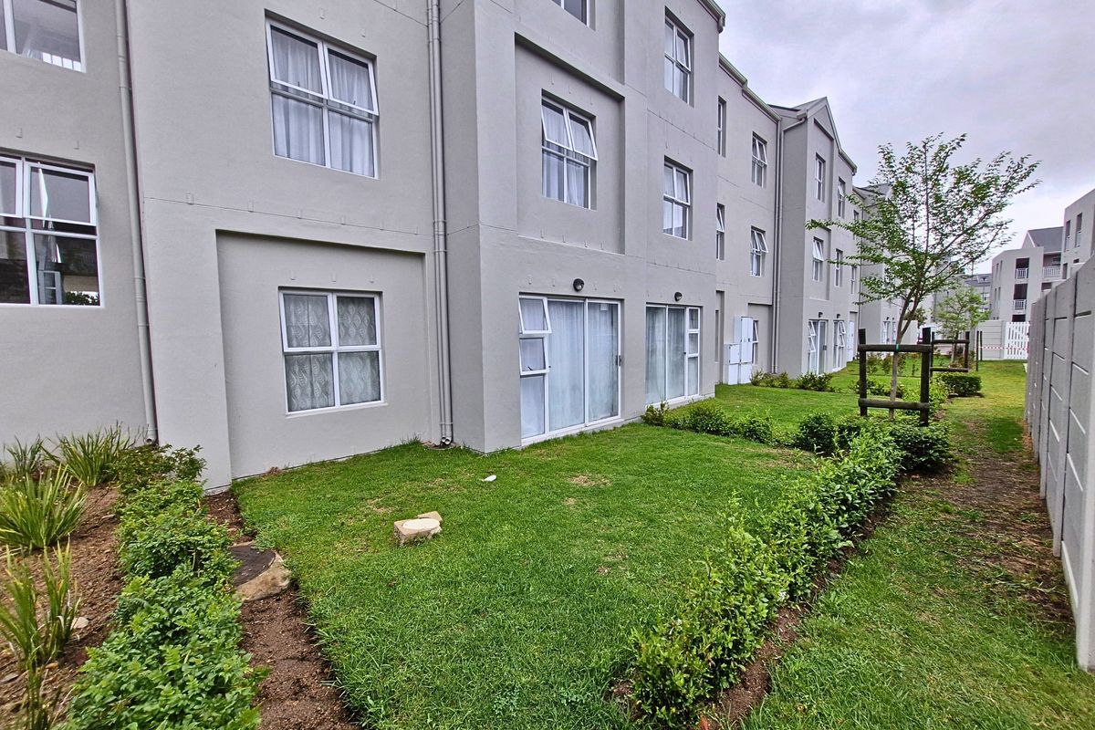 Rear view of a multi-story apartment complex featuring ground-floor units with sliding door access to a private garden area and boundary wall.