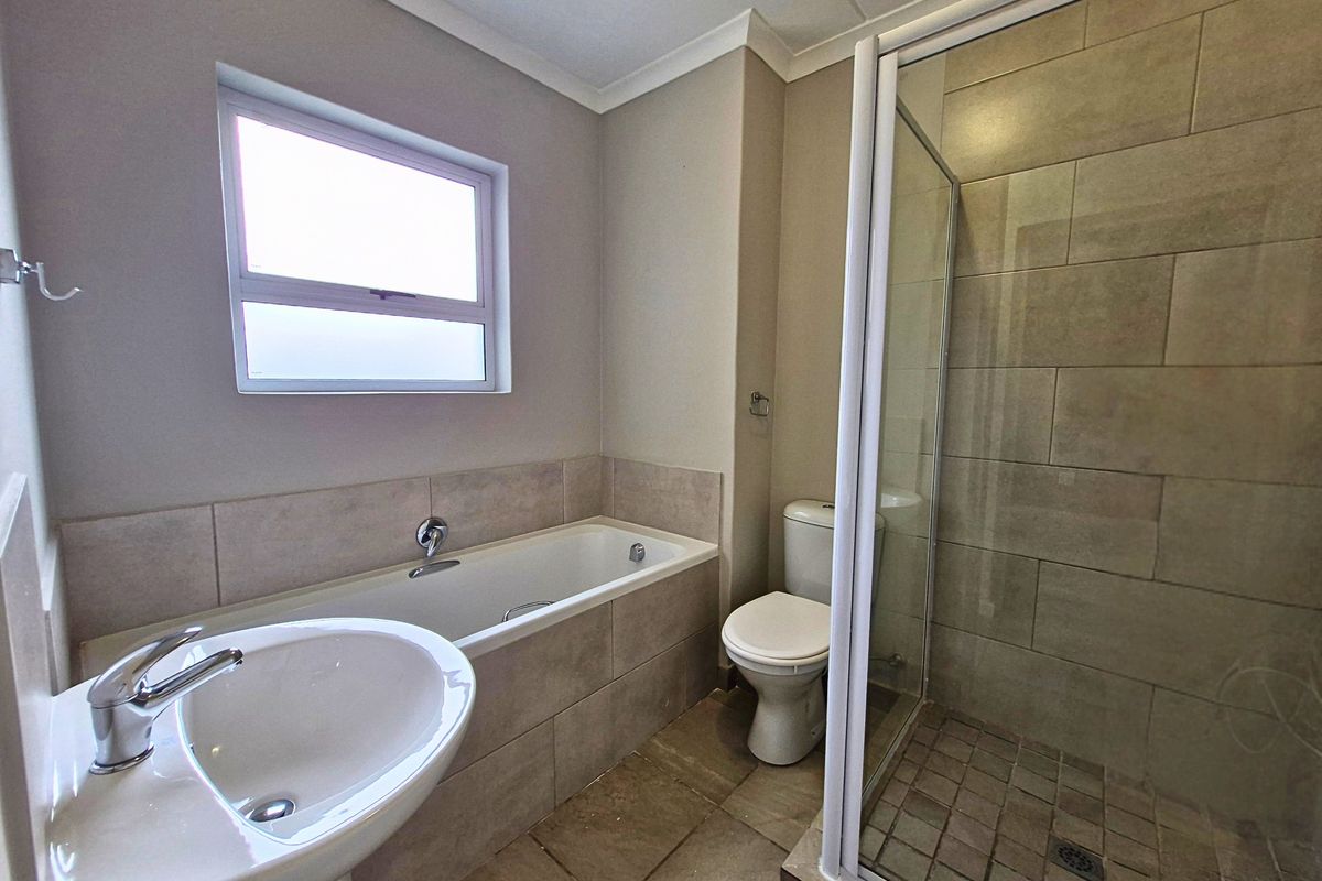 A clean, functional bathroom featuring a pedestal basin, built-in bathtub, separate shower enclosure, and neutral floor-to-ceiling tiling.