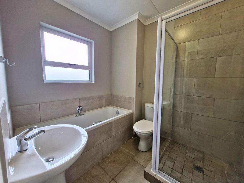 A clean, functional bathroom featuring a pedestal basin, built-in bathtub, separate shower enclosure, and neutral floor-to-ceiling tiling.