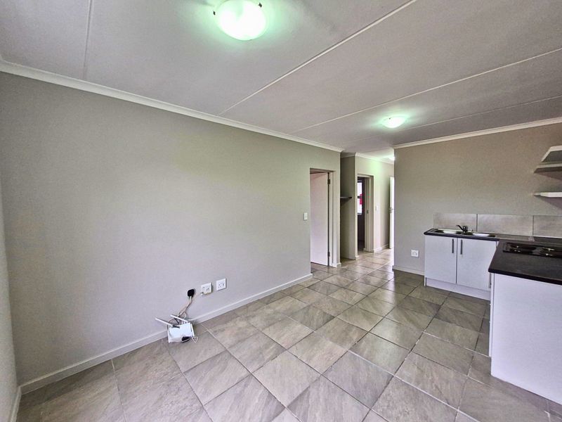 An open-plan living and kitchen area featuring neutral tiled flooring, built-in cabinetry, and a functional kitchen layout in a clean, vacant space.