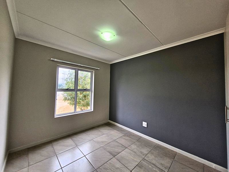 A clean, empty bedroom featuring neutral wall tones, a dark accent wall, tiled flooring, and a large window providing natural light.