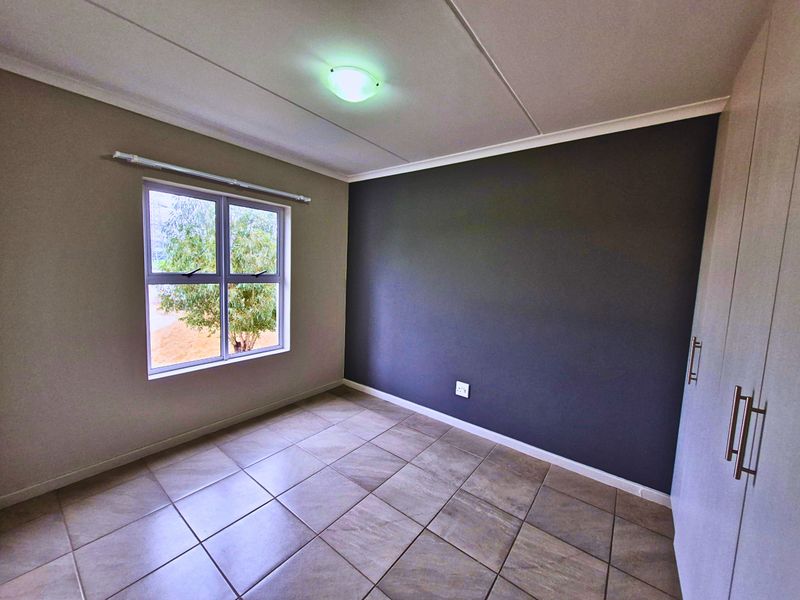 A clean, empty bedroom featuring tiled flooring, a dark accent wall, and built-in cupboards, offering a neutral canvas for personalization.