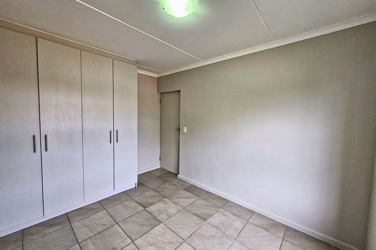 A clean, empty bedroom featuring neutral tiled flooring and ample built-in cupboard storage space.