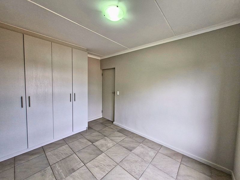 A clean, empty bedroom featuring neutral tiled flooring and ample built-in cupboard storage space.