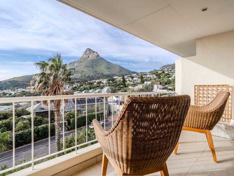 A spacious covered balcony featuring tiled flooring and a metal balustrade, offering expansive views of the surrounding landscape and mountain.