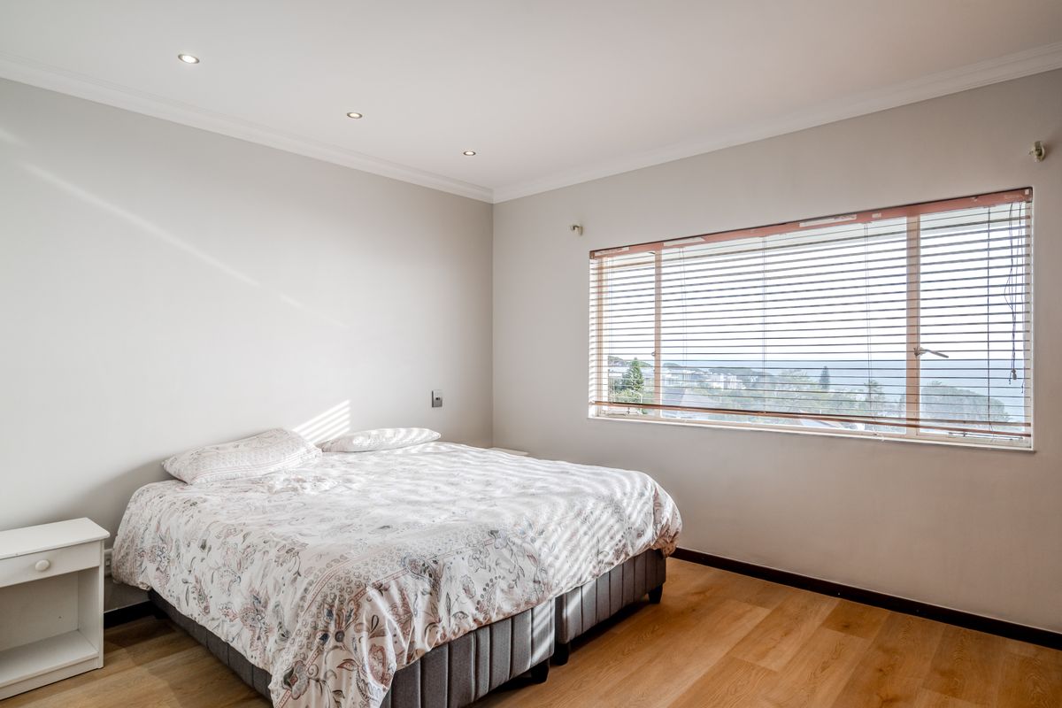 A bright and well-maintained bedroom featuring laminate flooring, recessed downlights, and large windows with venetian blinds offering a pleasant outlook.