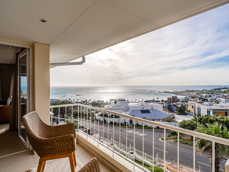 A spacious covered balcony featuring a metal balustrade and tiled flooring, offering expansive coastal and neighborhood views.