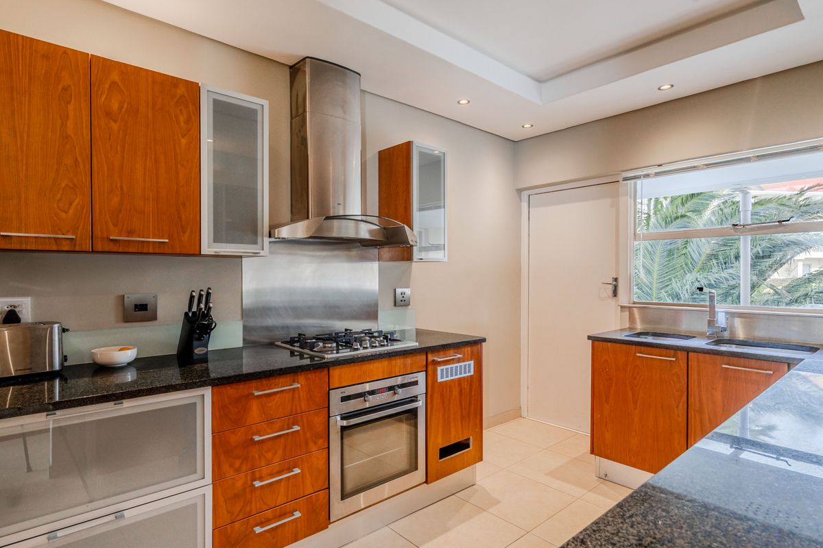 Modern kitchen featuring wood veneer cabinetry, granite countertops, stainless steel appliances, gas hob, and recessed lighting with a functional layout.