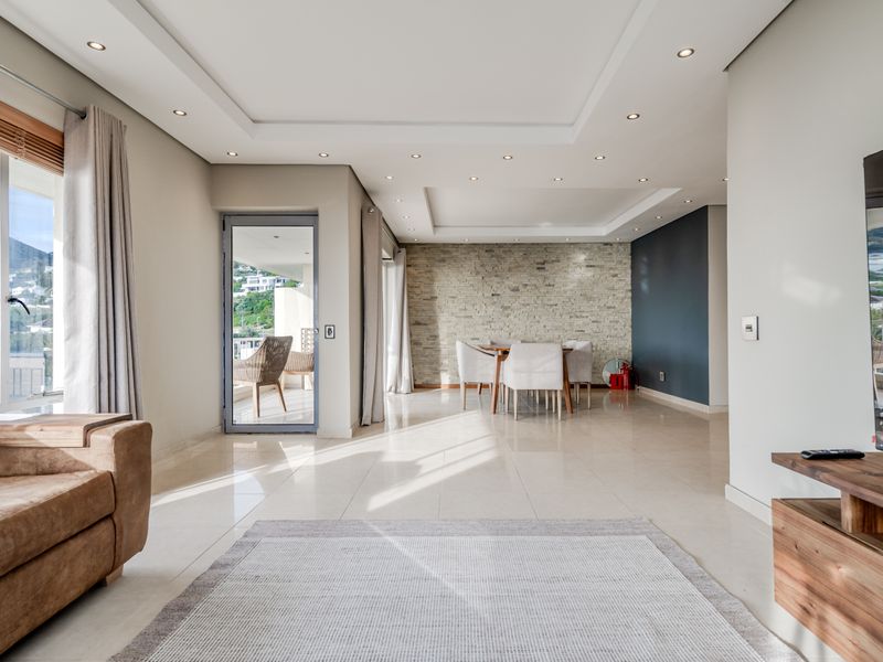 Spacious open-plan living and dining area featuring a modern stone accent wall, recessed ceiling lighting, and large glass doors leading to a balcony.