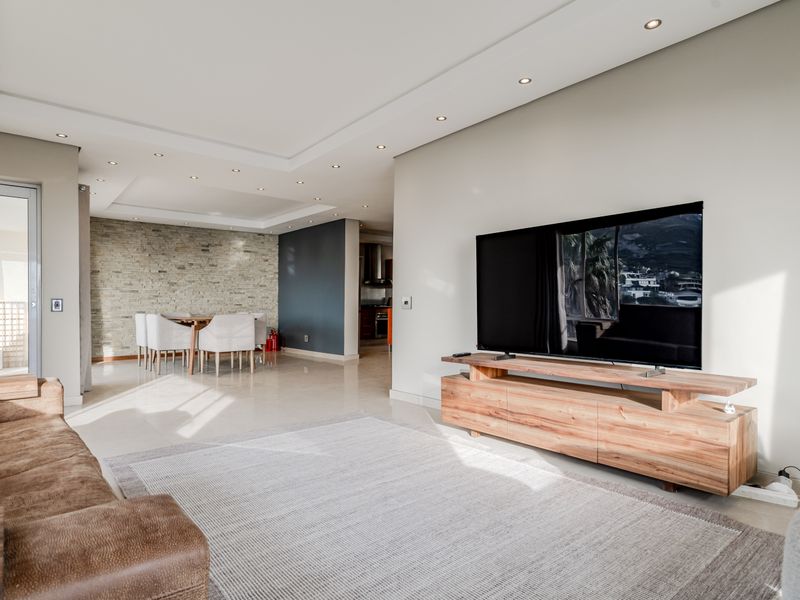 Spacious open-plan living and dining area featuring a stone accent wall, recessed lighting, and seamless access to an outdoor balcony.