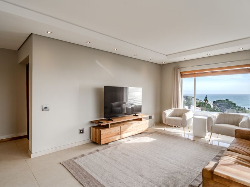 A bright and modern living room featuring tiled floors, recessed ceiling lighting, and a large window offering expansive ocean views.